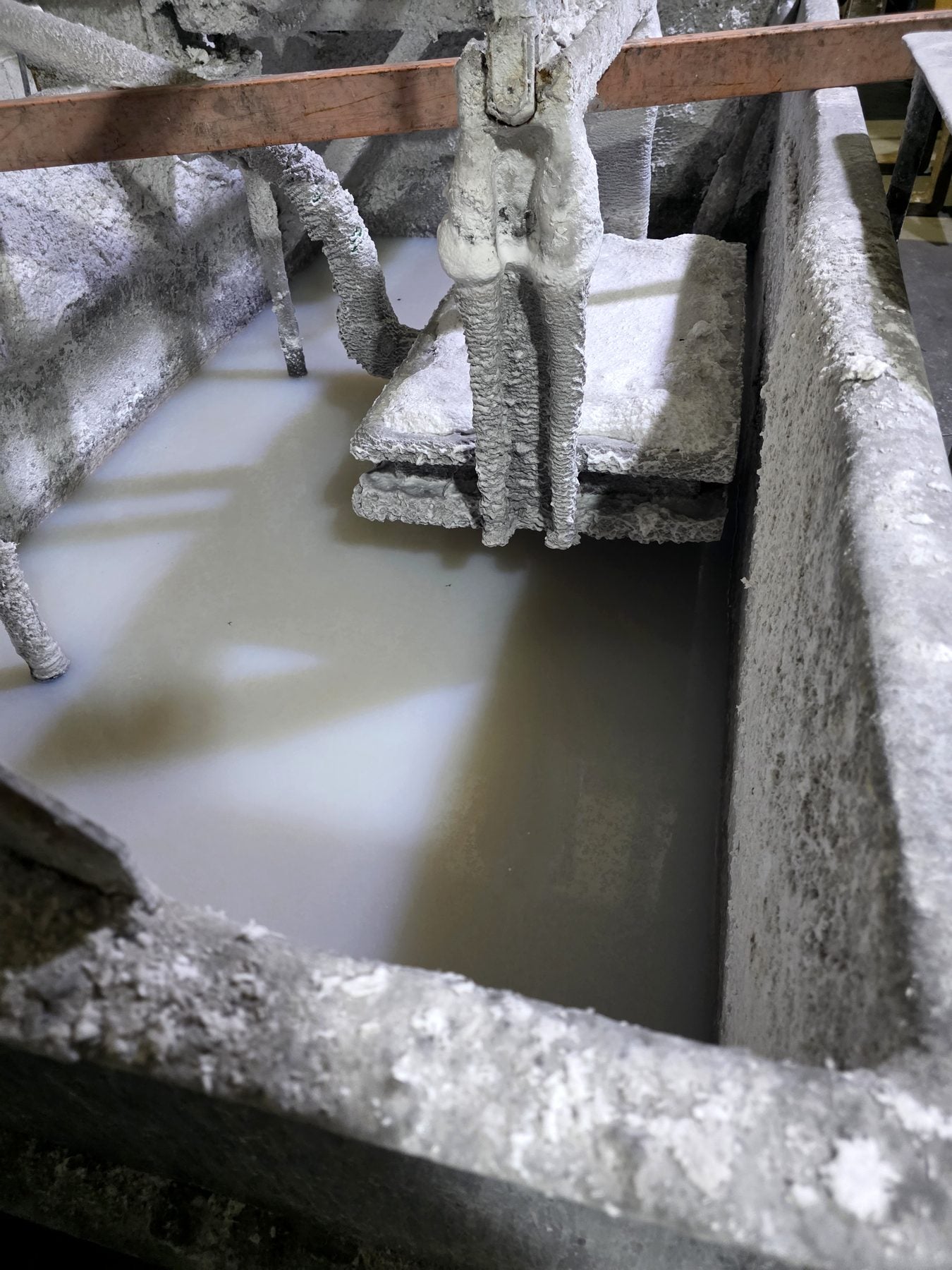 Bespoke coal-making machinery at The Stove Wizard in Flint, showing a workshop tank of ceramic slurry and equipment coated in ceramic residue.